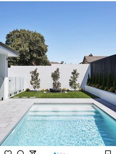 an empty swimming pool in front of a white fenced backyard with grass and trees