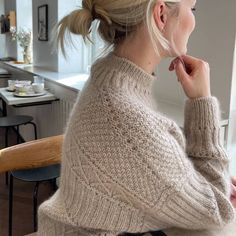 a woman sitting at a table with her hair in a pony tail bun, looking out the window