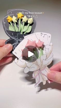 two hands are holding some paper flowers