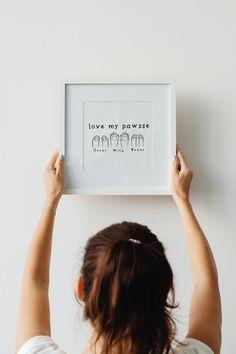 a woman holding up a framed art print with the words love my paws on it