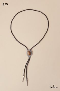 Tip your hat and up your aesthetic with the Petit Moments Western Wow Silver and Black Chunky Bolo Tie! This statement-making bolo tie has a woven faux leather cord with an adjustable, bolo-style toggle medallion at the front, which is composed of silver-toned metal and features an oversized, tiger's eye-like accent at the center. Matching embossed silver aglets complete the look. Adjustable bolo slide toggle. Necklace Measures 37" Long. 70% PU, 15% Zinc, 15% Quartz Stone. Imported. Lulus | West Bolo Tie Styling, Rodeo Lariat Bolo Tie With Adjustable Length, Adjustable Lariat Bolo Ties For Rodeo, Adjustable Length Lariat Bolo Ties For Rodeo, Adjustable Black Lariat Necklace, Black Adjustable Lariat Necklace, Western Style Adjustable Bolo Ties, Black Adjustable Bolo Tie, Adjustable Black Bolo Tie