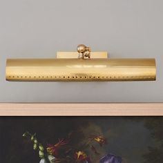 a painting on the wall next to a vase with flowers in it and a gold light fixture