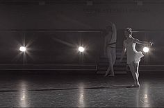 two ballerinas are performing in the dark with their arms extended and lights on