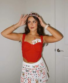 a woman in a red top and white skirt holding her hands up to her head