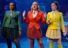 three girls in school uniforms stand on stage with their hands up to the air and look surprised