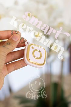 a hand holding a tiny ring with the letter o on it, in front of a floral arrangement