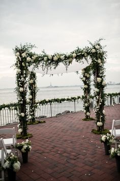 an outdoor ceremony set up with white flowers and greenery on the side of the water