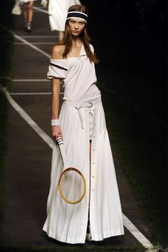 a woman with a tennis racket walks down the runway