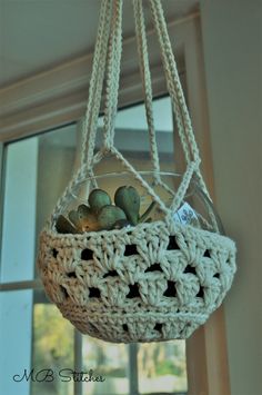 a crocheted hanging planter filled with succulents in front of a window