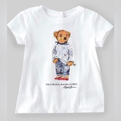 Polo By Ralph Lauren T-Shirt Features Cap Sleeves, Ribbed Crewneck, 3 Buttoned Placket At The Center Back, Straight Hem, Polo Mascot Bear By Ralph Lauren Dressed In Iconic Flag Sweater And Patchwork Jeans, Polo Bear By Ralph Lauren And Ralph Lauren Script At Front Chest Cotton T-shirt With Cartoon Print For Playwear, Cotton Tops With Letter Print For Playwear, Cotton Tops With Character Print For Playwear, White Short Sleeve T-shirt For Playtime, White Character Print Tops For Playtime, Cotton Crew Neck T-shirt For Playwear, Casual Tops With Cartoon Print For Playwear, Cotton Graphic Print Shirt For Playwear, White Tops With Character Print For Playtime