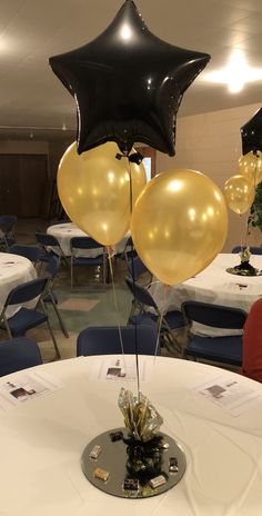 some black and gold balloons are on top of a white round table in a banquet hall