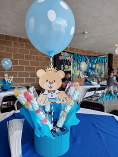 a teddy bear centerpiece in a blue box on a table with balloons and streamers