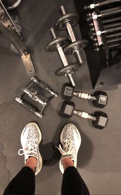 a person standing next to two dumbs and one weight machine with their feet on the ground