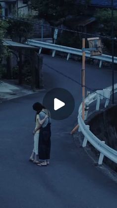 two people standing in the middle of an empty street at night, one person is holding his arm around the other