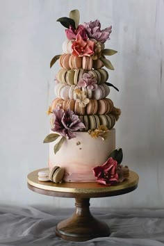 a three tiered cake decorated with flowers and macaroni shells on a stand