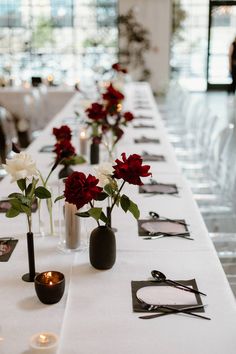 long table with white and red flowers in vases on each side, surrounded by candles