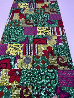 a very colorful piece of cloth with flowers and leaves on the bottom, sitting on top of a purple surface