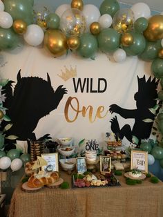 a table topped with cake and desserts under a wild one sign surrounded by balloons