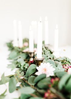 candles are lined up on a table with flowers and greenery