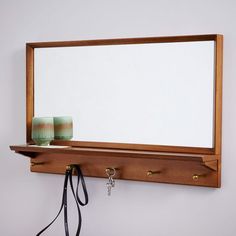 a mirror is hanging on the wall above a shelf with two cups and a pair of scissors