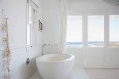 a large white bath tub sitting in a bathroom next to a window with an ocean view