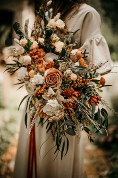 a woman holding a bouquet of flowers and greenery in her hands while standing outside