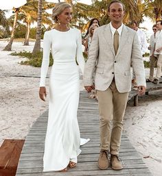 a man and woman walking down a wooden walkway on the beach with palm trees in the background