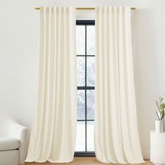 a living room with a white couch and large window covered in cream colored drapes