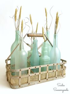 a basket filled with blue glass bottles and wheat stalks in it's centerpiece