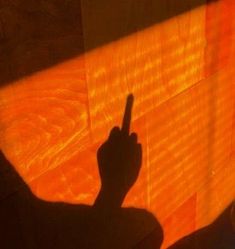 the shadow of a person's hand pointing at something on a wooden surface with orange light coming through it