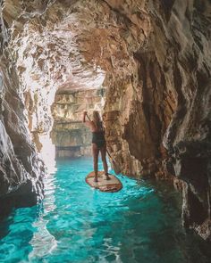 a woman standing on a surfboard in the middle of a cave with blue water