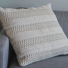 a white crocheted pillow sitting on top of a gray couch