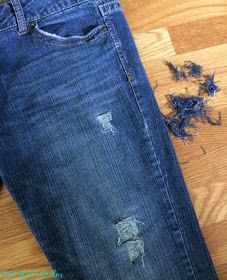 a pair of blue jeans with holes in them on a wooden floor next to a cell phone