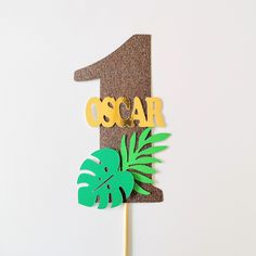 a cake topper with the number one on it and a green palm tree leaf