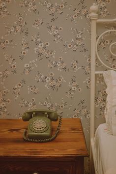 an old fashioned telephone sitting on top of a wooden table next to a wall papered with flowers