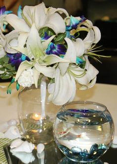 a vase filled with white and blue flowers on top of a table next to a fish bowl