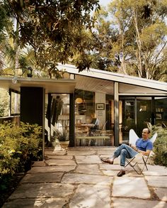 a man sitting in a lawn chair on top of a stone patio next to a house