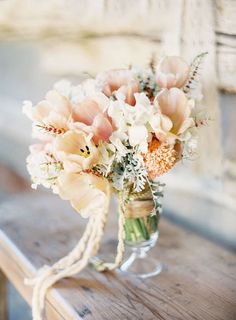 a bouquet of flowers in a mason jar on a wooden table with string tied around it