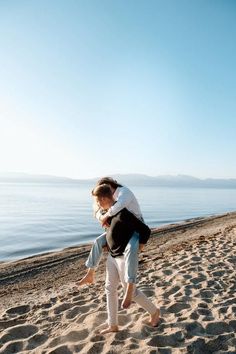 a man carrying a woman on his back while walking along the sand at the beach