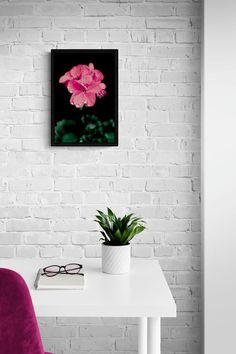 a pink flower sitting on top of a white table next to a purple chair and potted plant