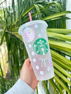 a person holding up a starbucks cup in front of a palm tree