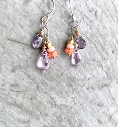 "Iolite Sunstone Earring Tiny gemstones are wire wrapped and dangle enticingly in vivid, natural color. Pink amethyst briolettes swing next to drops of violet iolite and wee stacks of sunstone and pink opal. Delicate and detailed, meticulously crafted. For those of us who L-O-V-E little gemstones. In sterling and oxidized silver, and 14k gold fill. GEMSTONES: Pink amethyst (lavender) - faceted briolettes - 9mm Iolite - faceted briolettes - 7mm Sunstone - faceted rondelles - 4mm Pink opal - facet Sunstone Earrings, Purple Gemstones, Earring Silver, Pink Amethyst, Cluster Earrings, Pink Opal, Gold Plated Silver, Orange And Purple, Wire Wrapped