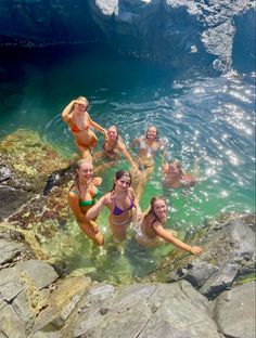 several women in bikinis are swimming in the water near rocks and icebergs