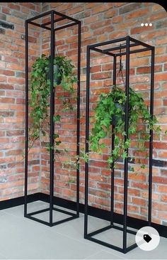 three black metal planters with plants growing in them against a brick wall and floor