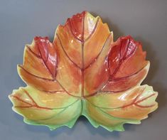 an orange and green leaf shaped dish on a gray surface with grey wall in the background