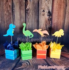 four different colored paper dinosaurs in small boxes