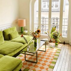 a living room filled with green furniture and flowers on top of a coffee table in front of an arched window