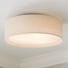 a light fixture in a white room with a beige lamp shade on the ceiling above it