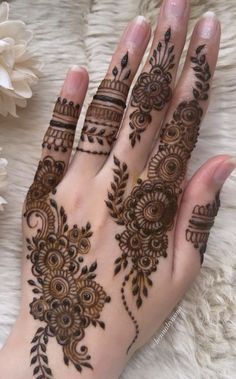 a woman's hand with henna tattoos on it and flowers in the background