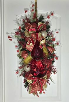 a red and gold christmas wreath hanging on the front door with ornaments around it's edges